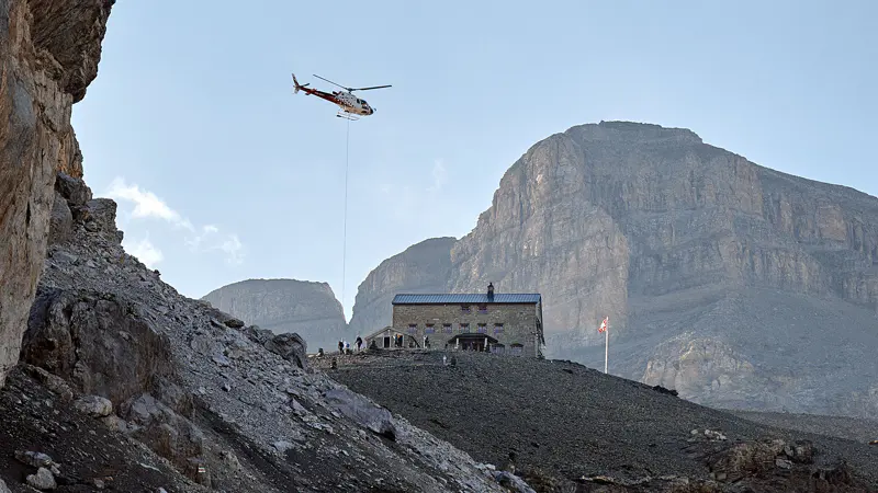 Een helikopter die boven een berghut zweeft.